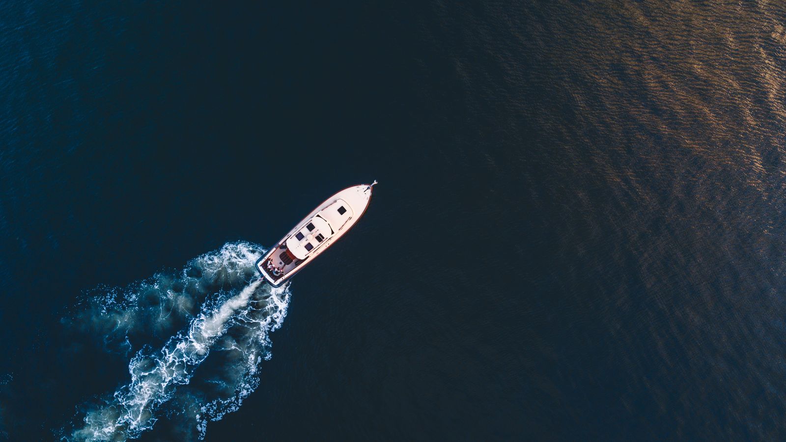 Aerial view of a yacht's wake curving across dark open water
